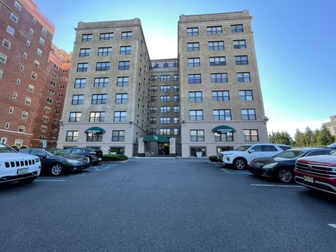 A parking lot in front of a multi-story building with cars parked.