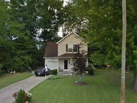 A house with a white door and windows is surrounded by greenery.