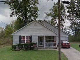 A small house with a porch and a car parked in front.