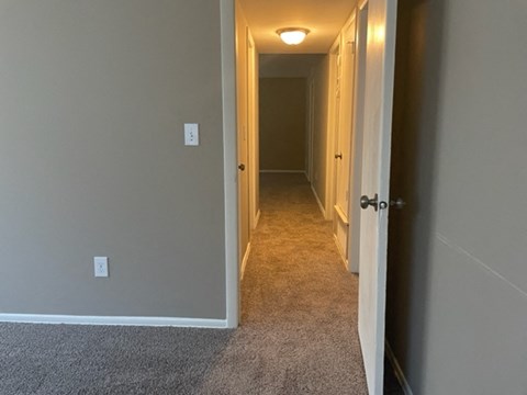a hallway with a carpeted floor and a door to a bedroom and a hallway