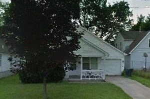 A white house with a porch and a tree in front.