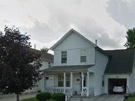 A white house with a porch and a car in the driveway.