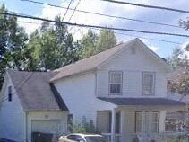A white house with a black roof and a car parked in front.