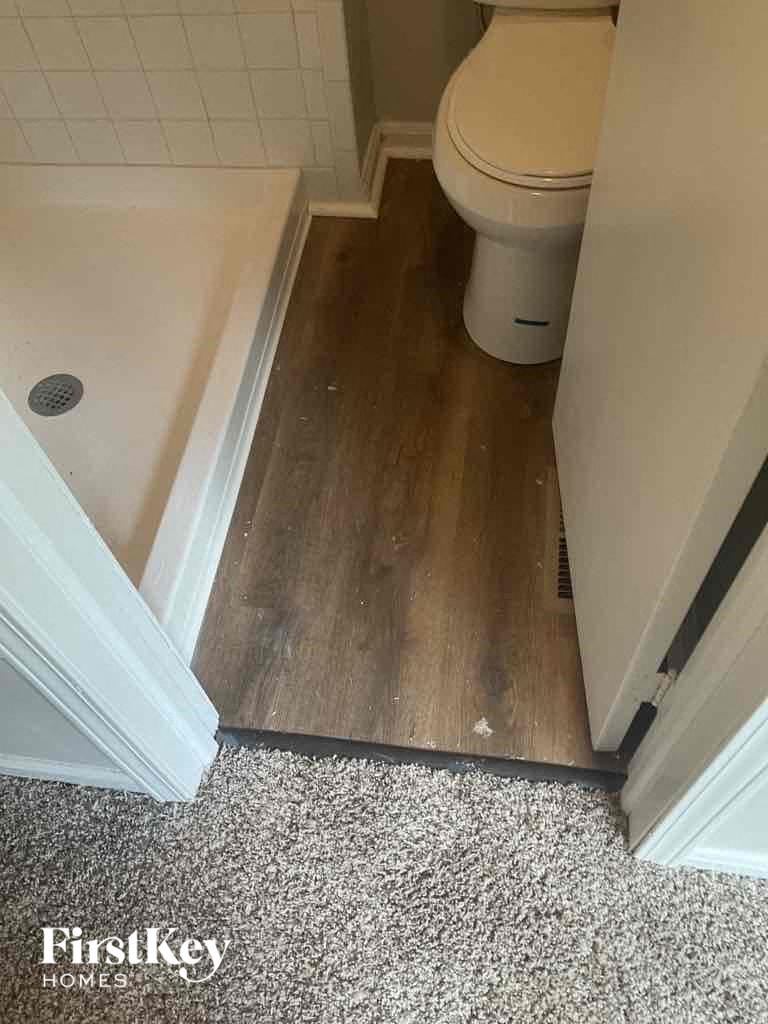 A white toilet in a small bathroom with a wooden floor.