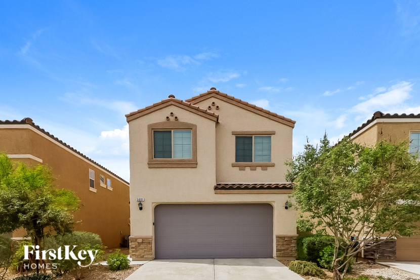 A beige house with a garage door and a tree in front.