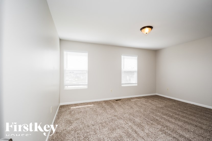 A room with a carpeted floor and two windows with blinds.