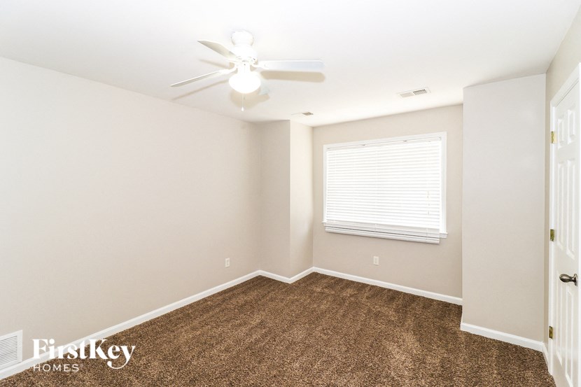 A room with a carpeted floor, a ceiling fan, and a window with blinds.