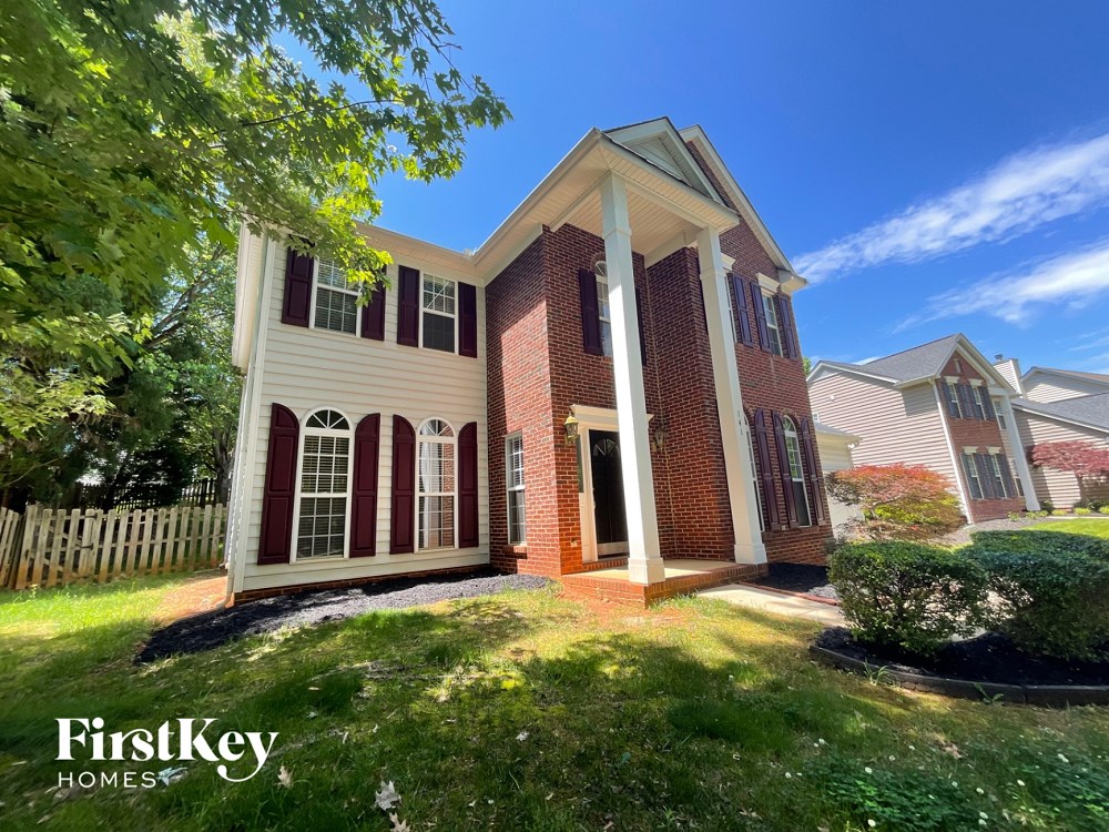 A brick house with a white porch and a tree in front.