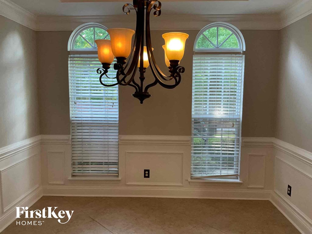 A chandelier hangs over a window in a room with white walls and a beige floor.