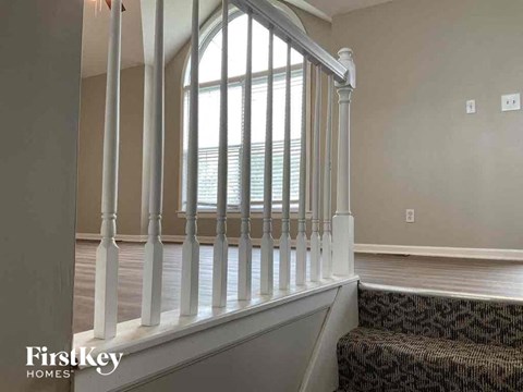 A staircase with a carpeted runner and white balusters leads to a window.