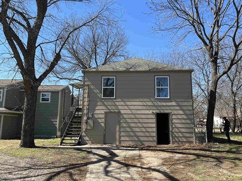 A small house with a grey roof and a black door is surrounded by bare trees.