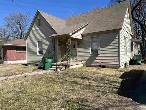 A house with a grey roof and a green trash can in front.