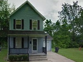 A green house with a porch and a covered walkway.