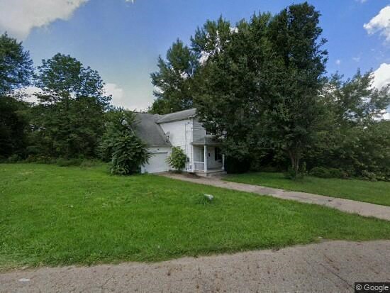 A white house with a grey roof is surrounded by a green lawn.