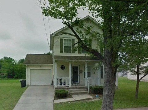 A house with a white porch and a tree in front.