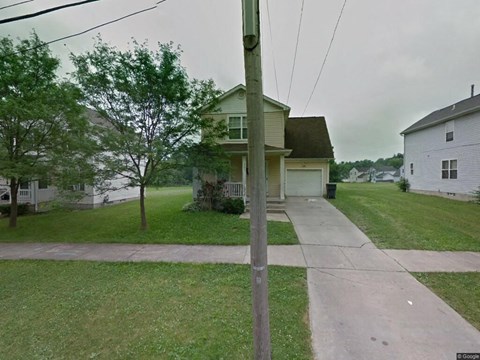 A house with a green lawn and a grey house in the background.