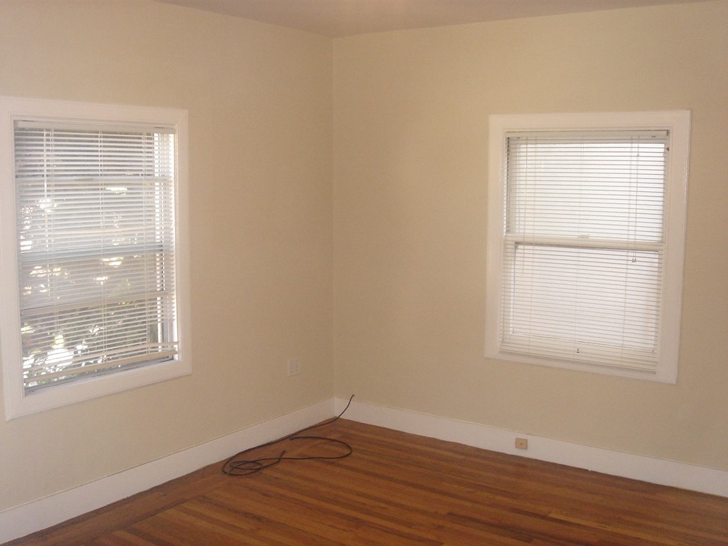 the corner of a room with two windows and a wooden floor