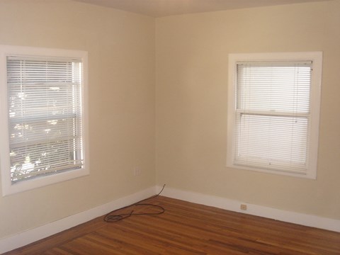 the corner of a room with two windows and a wooden floor
