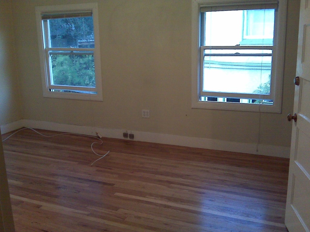 an empty living room with wooden floors and two windows