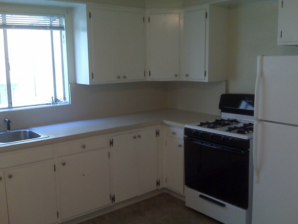 an empty kitchen with white cabinets and a stove and refrigerator