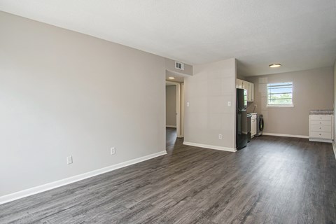 an empty living room and kitchen with wood floors and white walls