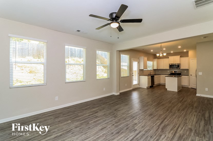 an empty living room with a ceiling fan and a kitchen