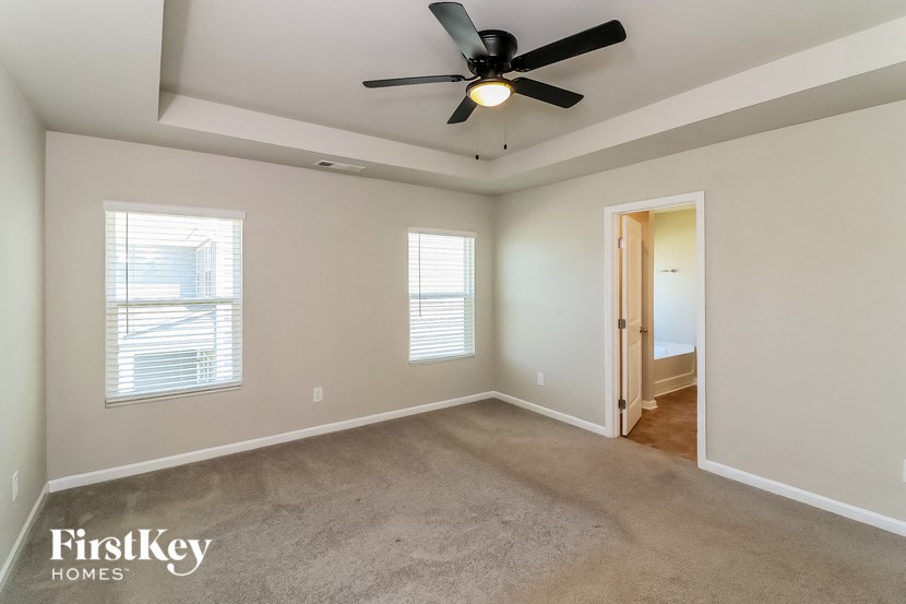 an empty living room with a ceiling fan and a door to a hallway
