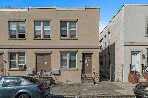 A grey car is parked in front of a brown building.