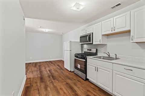 A kitchen with white cabinets and a wooden floor.