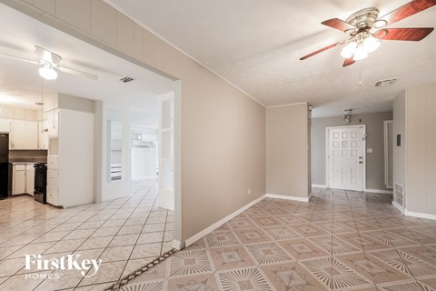 an empty living room with a ceiling fan and a kitchen