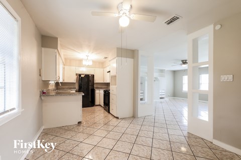a kitchen with white cabinets and tiled floors and a black refrigerator