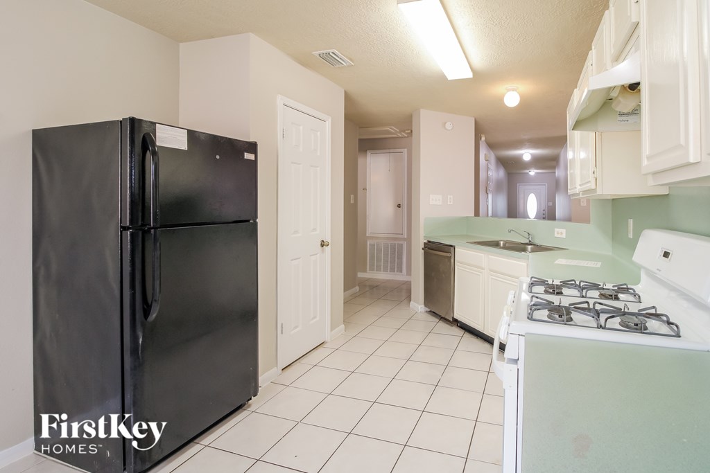 A black refrigerator is in a kitchen with white cabinets.