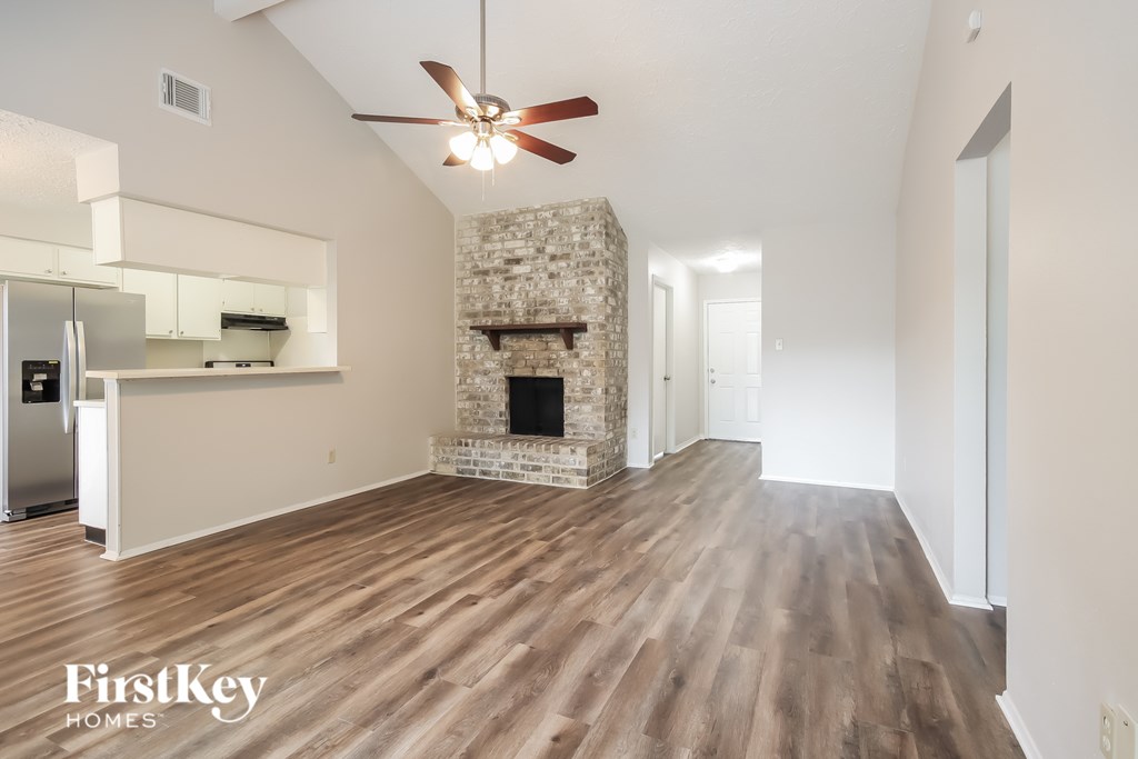 A spacious room with a stone fireplace and wooden flooring.