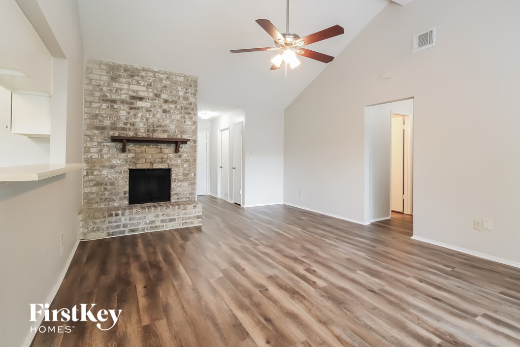 A spacious room with a stone fireplace and wooden flooring.