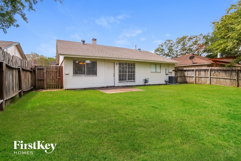 A white house with a brown roof and a fence surrounding a green lawn.