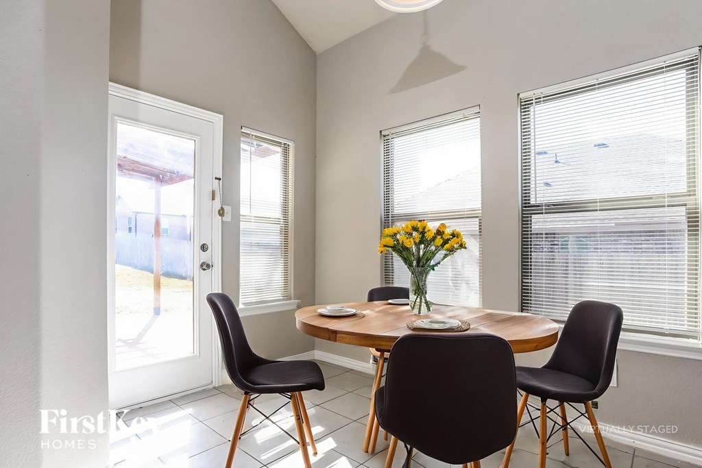 A dining room with a table, chairs and a vase of flowers.
