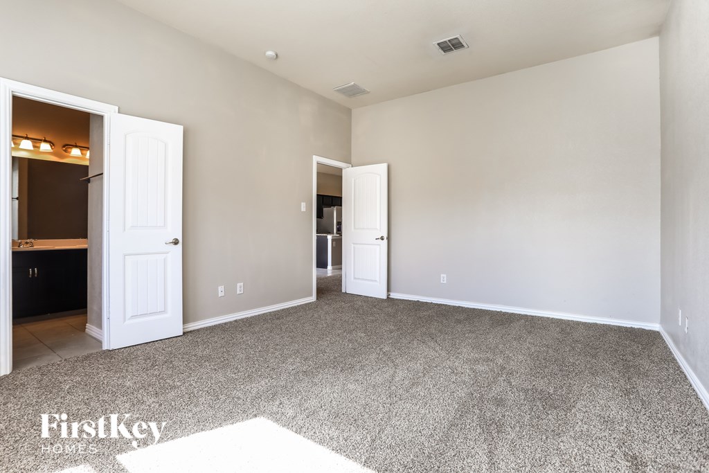 A spacious room with a carpeted floor and two doors, one of which is open to a kitchen.