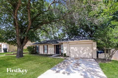 A house with a garage is surrounded by trees and has a driveway leading to the front door.