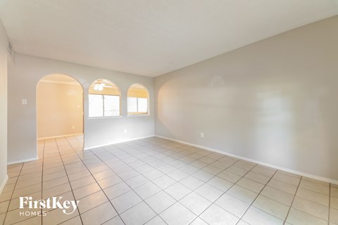 A spacious room with white walls and tile flooring, featuring three arched windows.