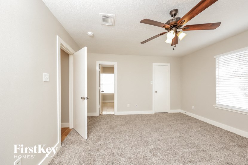 an empty living room with a ceiling fan and a door to a bathroom