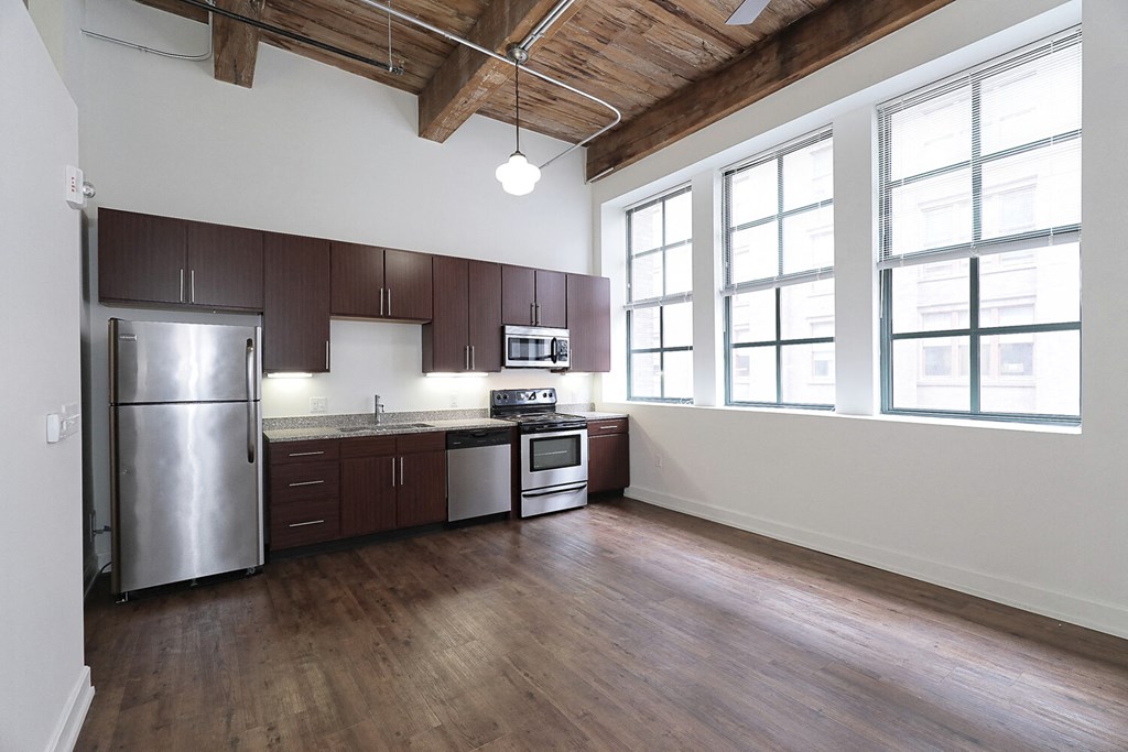 an empty kitchen with wood floors and a stainless steel refrigerator
