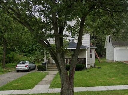 A tree in front of a white house with a car parked on the street.
