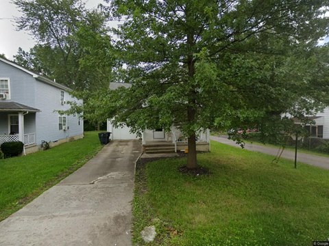 A tree in a front yard with a house in the background.
