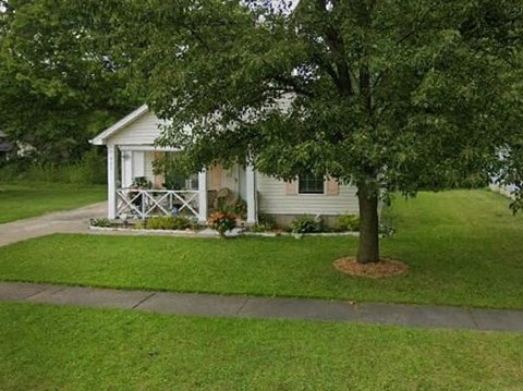 A small white house with a porch and a tree in front.
