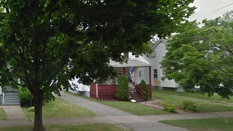 A house with a flag on the front porch is surrounded by trees.