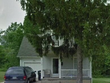 A white house with a blue car parked in front.