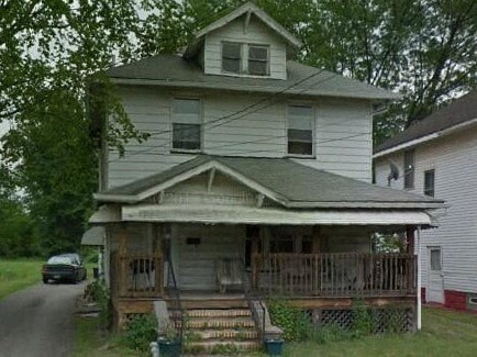 A white house with a porch and a car parked in front.