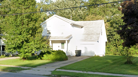 A white building with a garage door is surrounded by greenery.