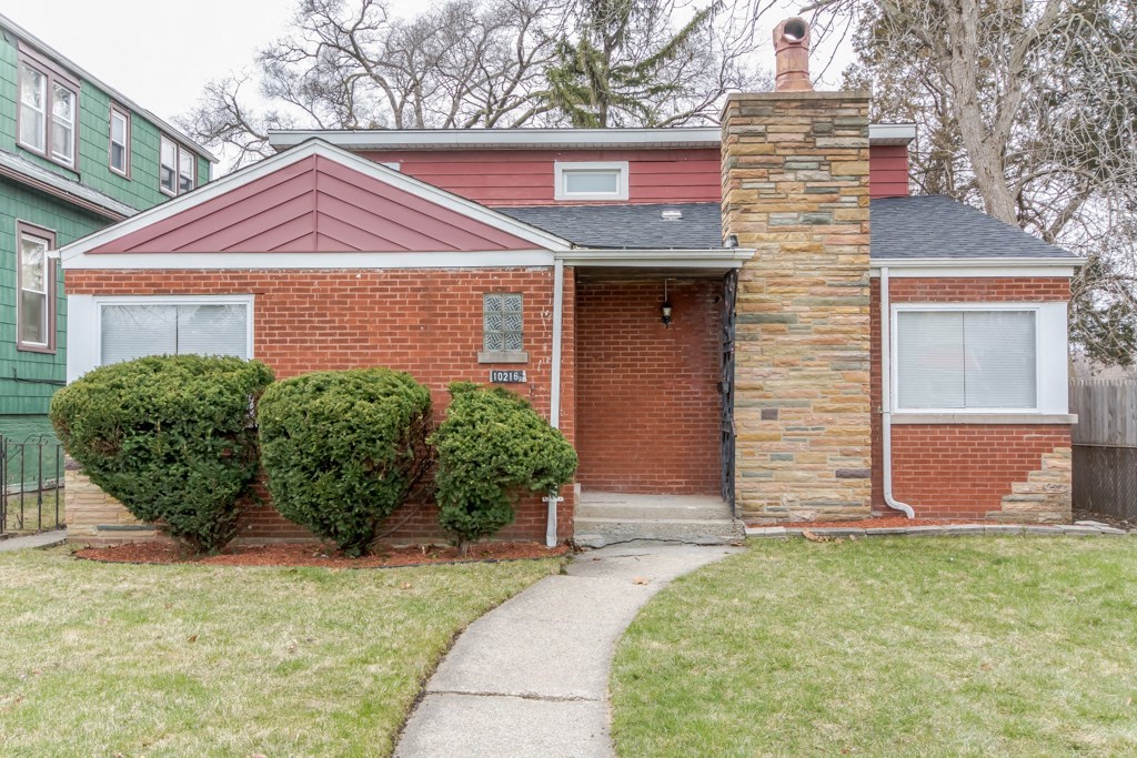 A red brick house with a chimney and a green house next to it.