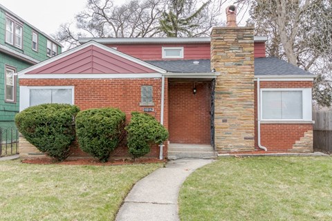 A red brick house with a chimney and a green house next to it.
